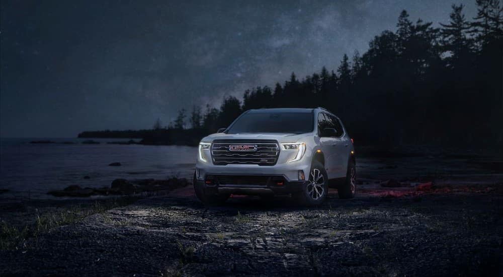 A white 2024 GMC Acadia AT4 is shown near a lake at night after visiting a GMC dealer.