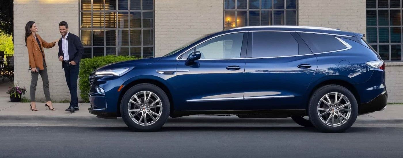 Blue 2023 Buick Enclave parked on the street with a couple standing nearby.