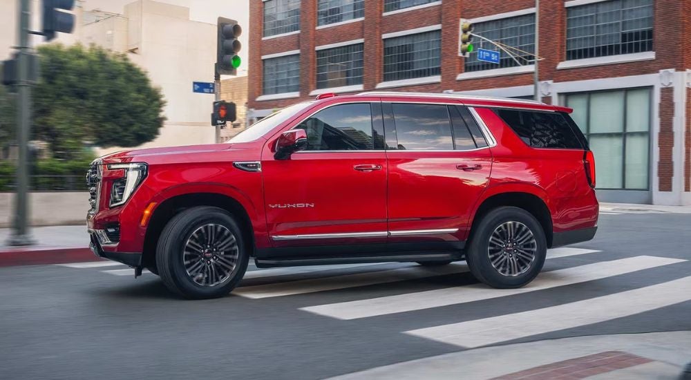Red 2027 GMC Yukon Elevation driving through an intersection.