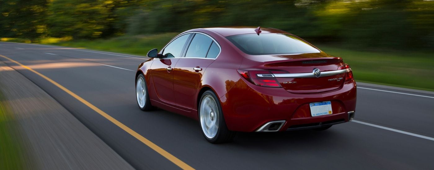 A red 2014 Buick Regal GS is shown driving on a tree-lined road after visiting a Buick dealer near Brighton.