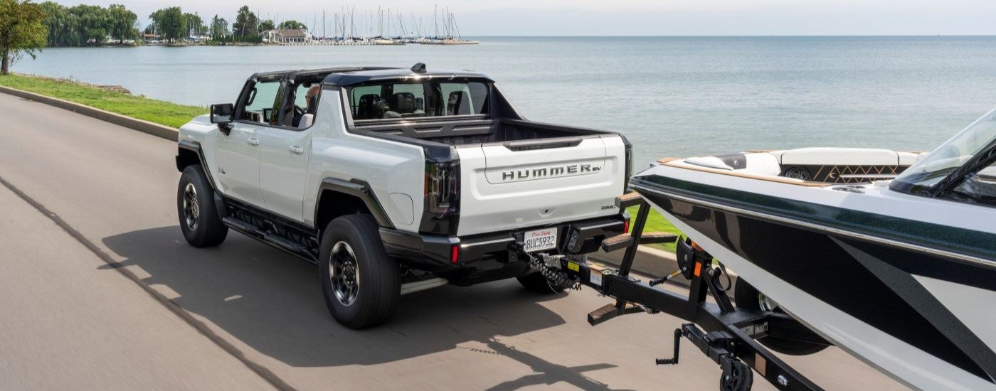 A white 2023 GMC Hummer EV is shown towing a boat past a lake.