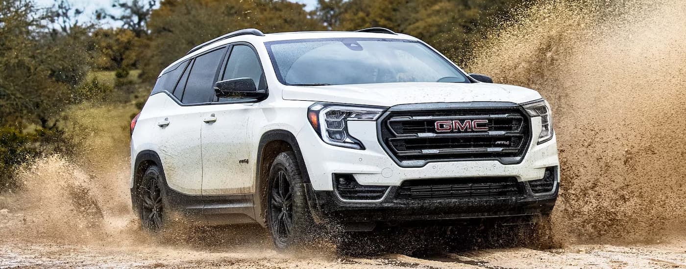 A white 2024 GMC Terrain AT4 is off-roading on a sandy trail.