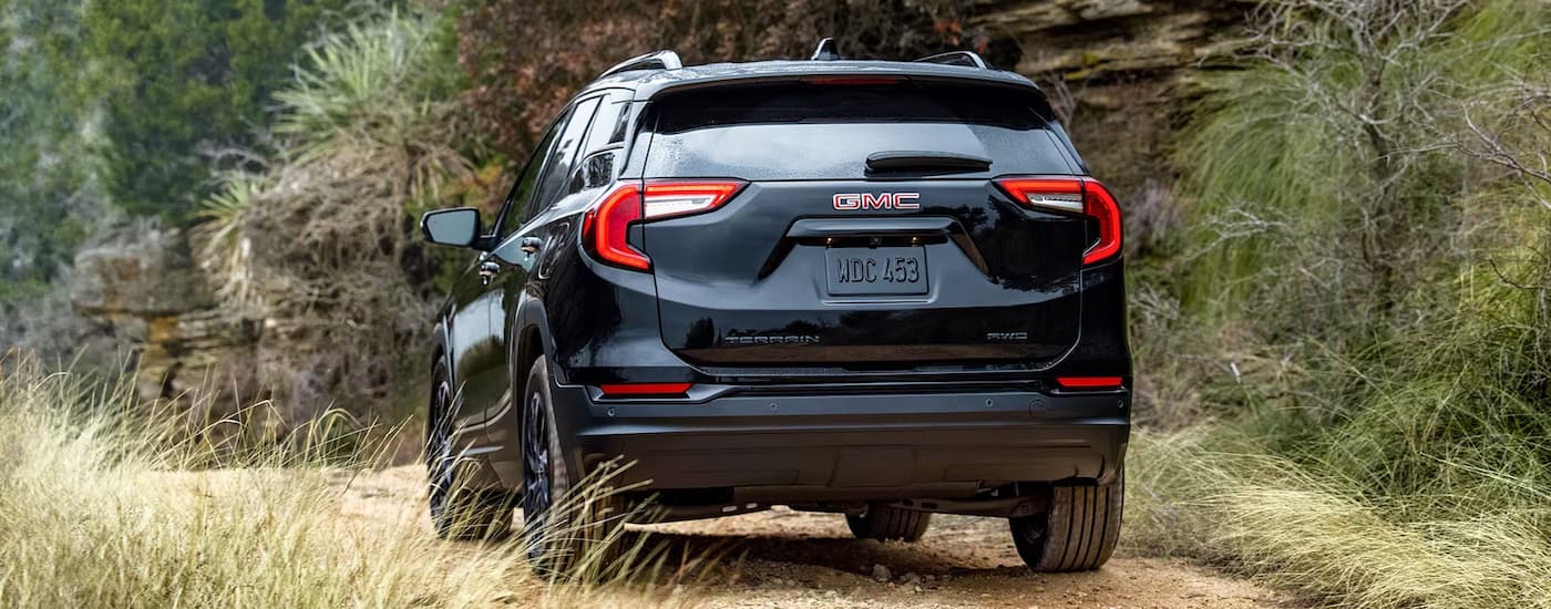 A black 2024 GMC Terrain SLT is shown from the rear on a dirt road.