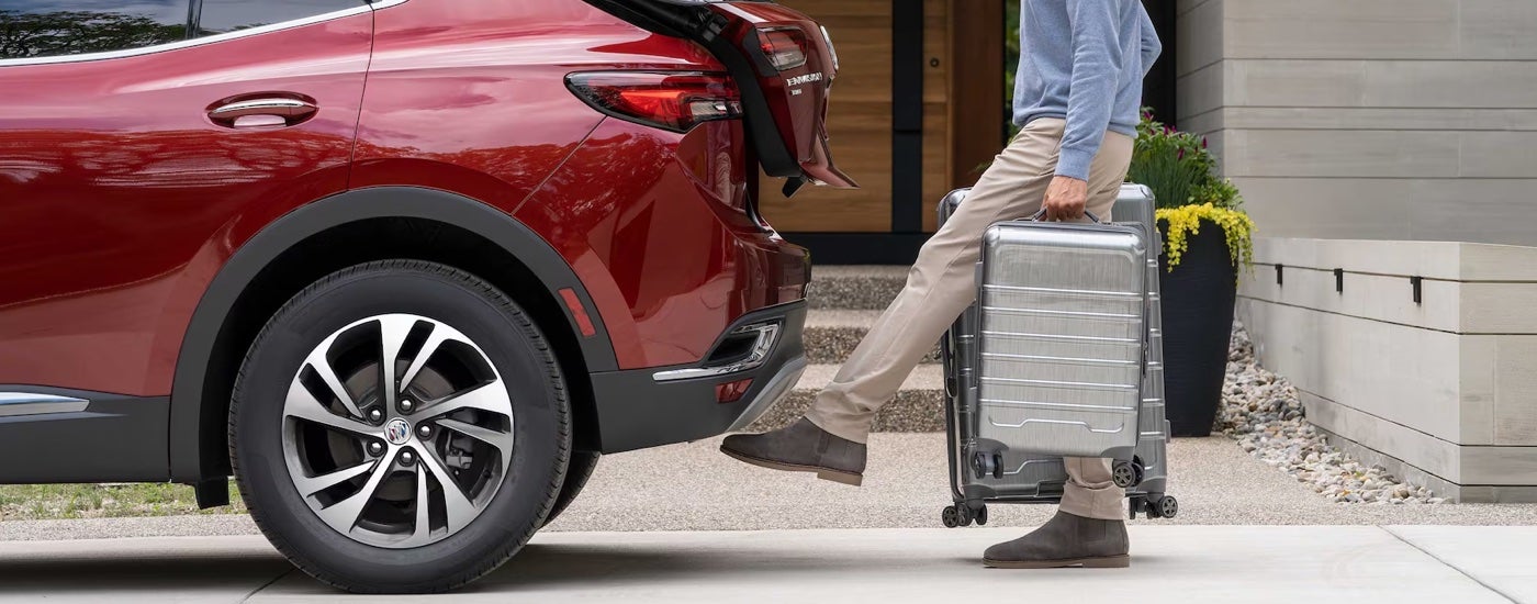 A man using his foot to activate the power liftgate on a red 2023 Buick Envision at a used Buick dealer near Canton.