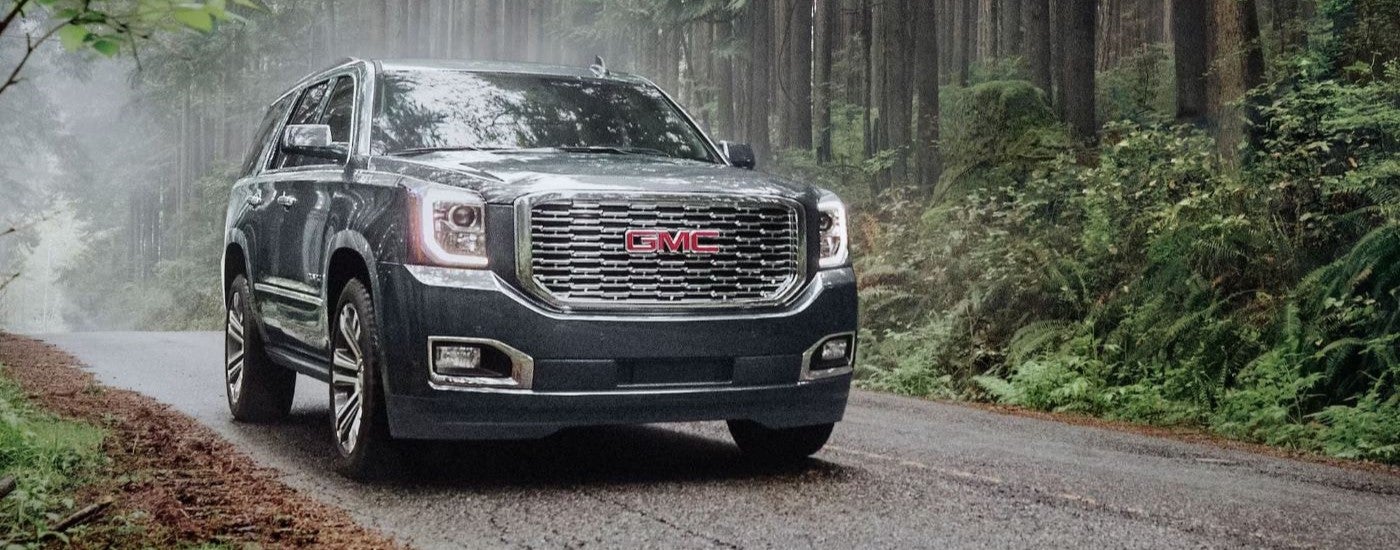 A grey 2020 GMC Yukon Denali driving through a forest.